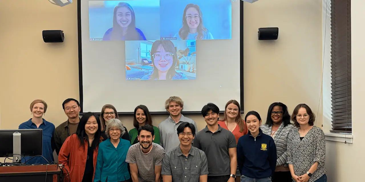 Faculty and graduate students from Purdue’s Industrial-Organizational Psychology program posing together in a classroom, with some members joining virtually on screen.