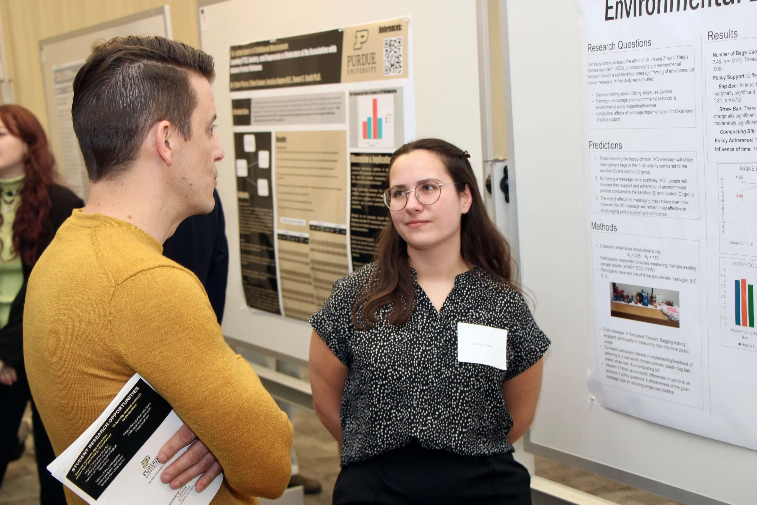 Sophia listening to a person while standing in front of her poster.